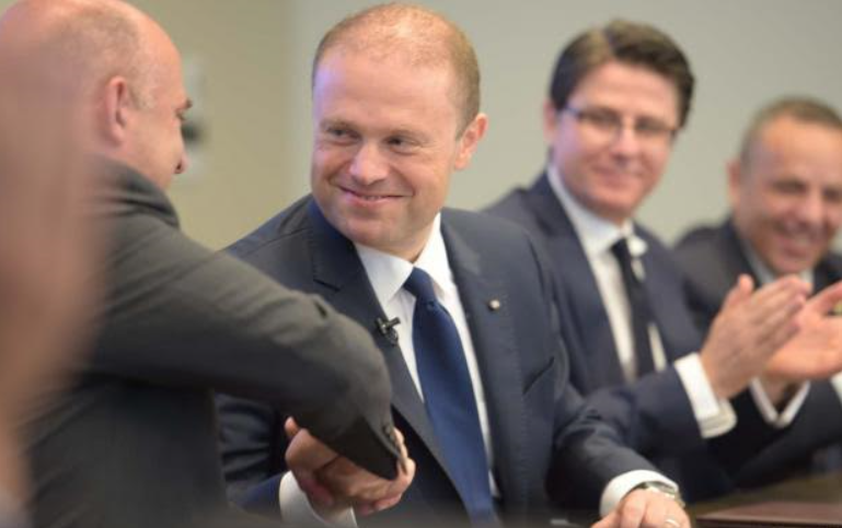 A delighted Keith Schembri, owner of secret money-laundering companies in Panama, the British Virigin Islands, Gibraltar and Cyprus. looks (far right) as the Prime Minister shakes on the deal with a Crane Currency executive.