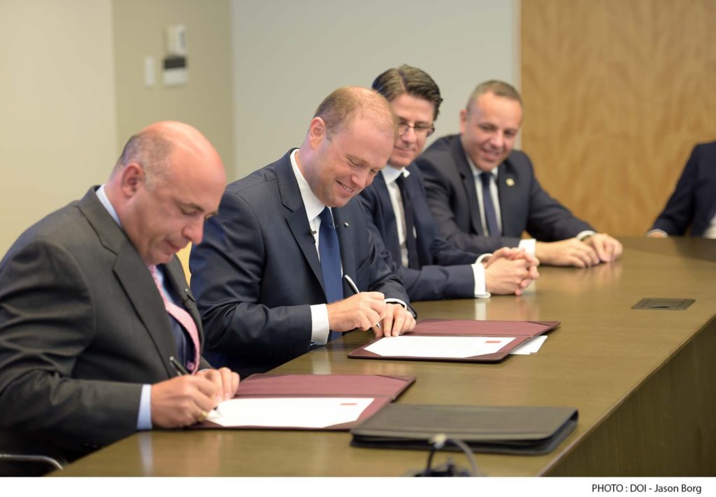 Joseph Muscat signs a deal with Crane Currency, on behalf of the government of Malta, while his chief of staff Keith Schembri (far right) looks on. 